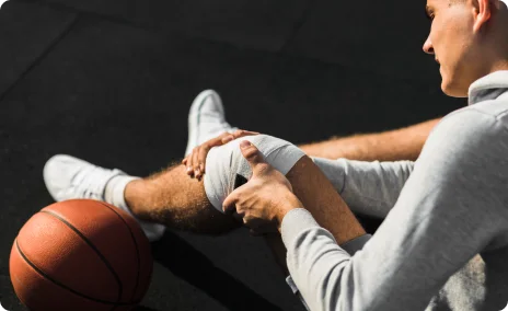 Basketball player holding an injured knee while sitting on the court.